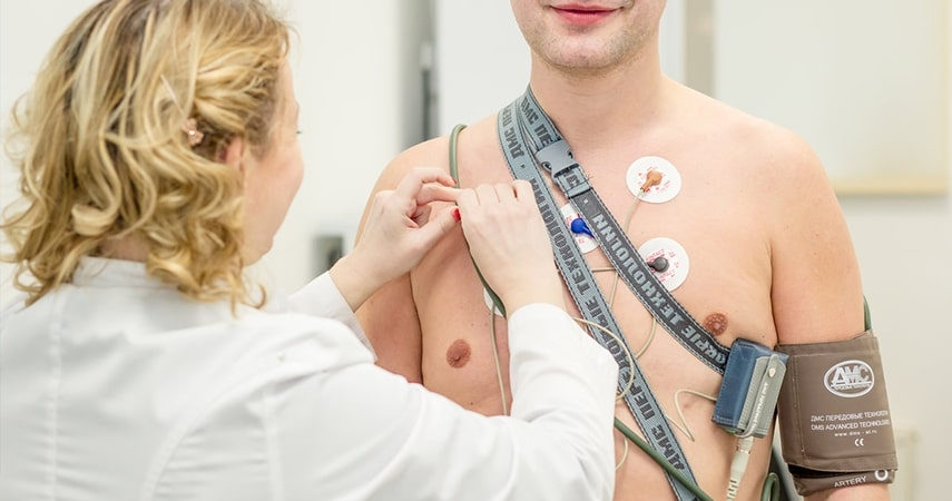 A healthcare professional prepares a male patient for an electrocardiogram (EKG) by placing electrodes on his chest.